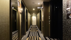 Een hotelgang met een patroon in het tapijt, meerdere deuren en een plafondlamp.