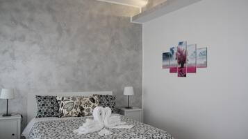 Camera d'albergo moderna con parete grigia strutturata, un letto con copripiumino a motivi floreali, due comodini con lampade e un'opera d'arte appesa al muro.