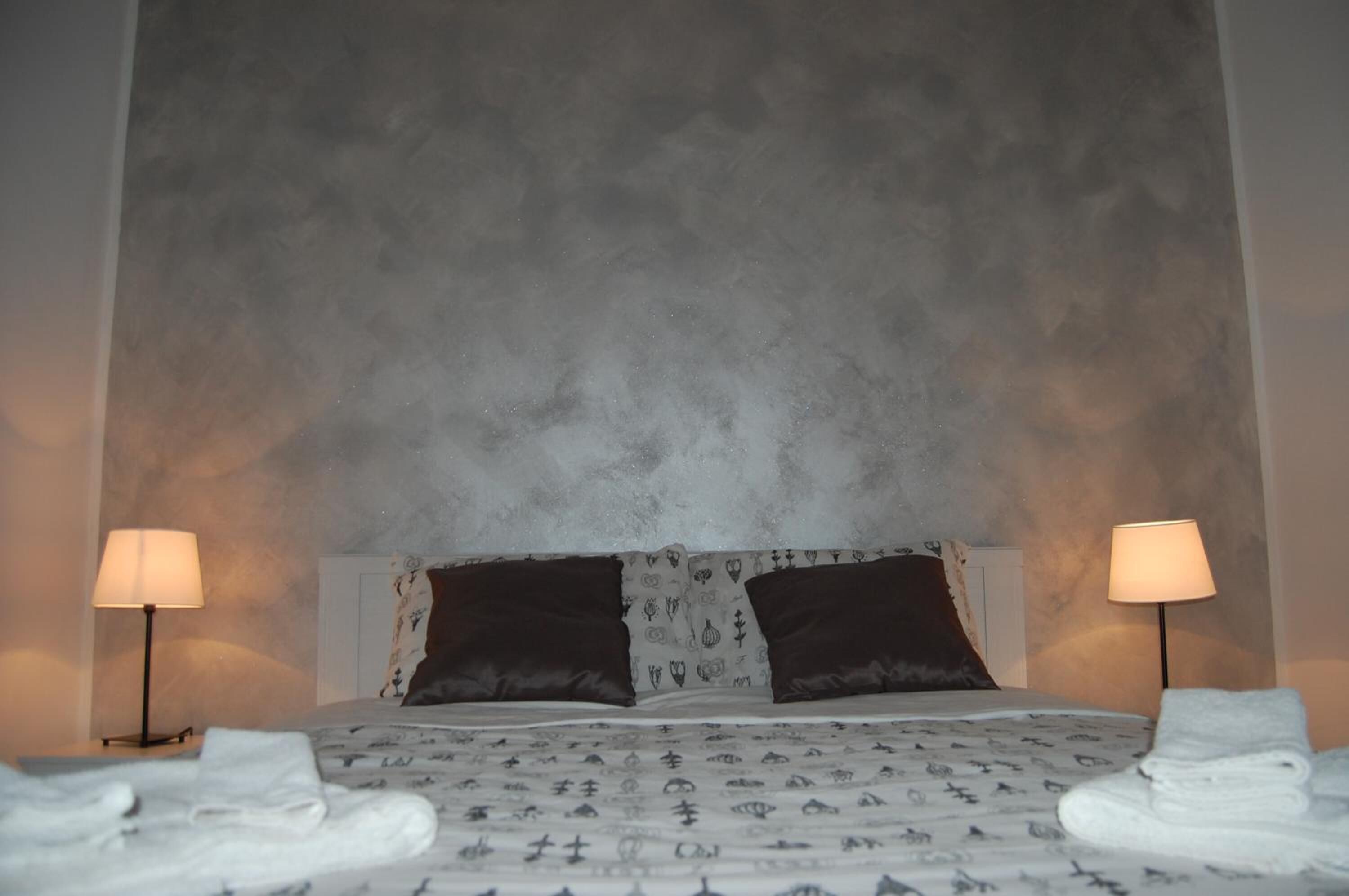 Un letto con una coperta a motivi, due cuscini scuri e due abat-jour.
