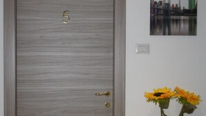 Uma porta com o número 5, um vaso com girassóis e uma pintura de paisagem urbana na parede.
