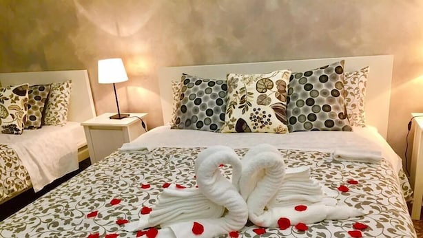 Quarto de hotel com cama adornada com arranjo de toalha em formato de cisne e pétalas de rosa. Há duas mesas de cabeceira, cada uma com uma luminária. O quarto tem uma paleta de cores neutras com roupa de cama estampada.