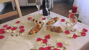 Mesa posta com pratos de comida, copos de vinho e pétalas de rosas espalhadas.