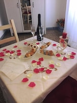 Mesa posta com pratos de comida, copos de vinho e pétalas de rosas espalhadas.