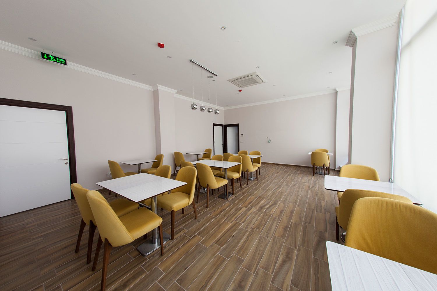 A conference room with yellow chairs and tables, white walls, and a wooden floor.