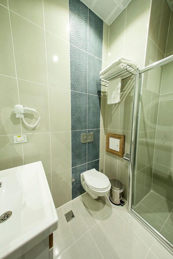 Un baño con inodoro blanco, cabina de ducha con mampara de vidrio y lavabo con espejo.
