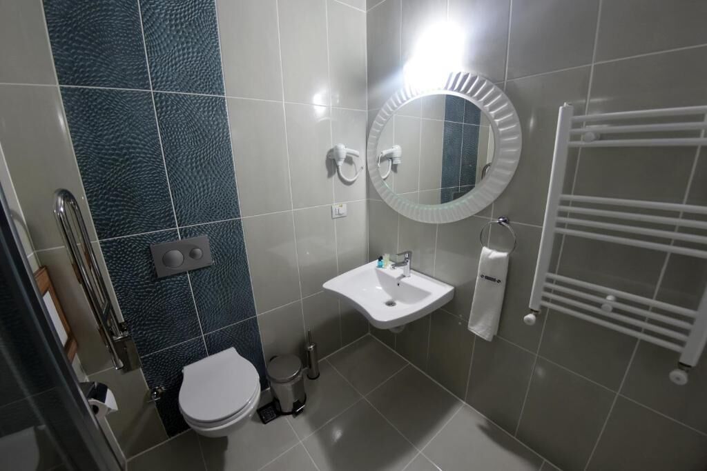 A compact bathroom with a toilet, sink, mirror, towel rack, and a hand dryer.