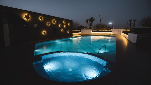 Une piscine avec un jacuzzi, entourée d’un mur sombre orné de motifs de feuilles illuminés.