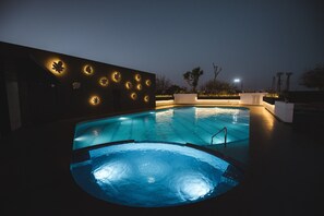 Una piscina con un jacuzzi, rodeada por un muro oscuro con diseños de hojas iluminados.
