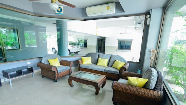 A modern living room with wicker furniture, a glass coffee table, and large windows offering a view of the outside. - BJ Boutique (Rayong)