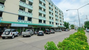 A multi-story hotel with a flat facade, several balconies, and a parking lot with various vehicles. - BJ Boutique (Rayong)