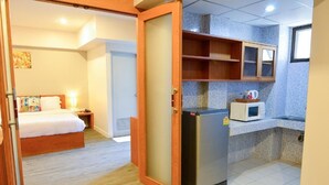 A hotel room with a bed, a wooden door, a kitchenette with a microwave, and a small cabinet. - BJ Boutique (Rayong)