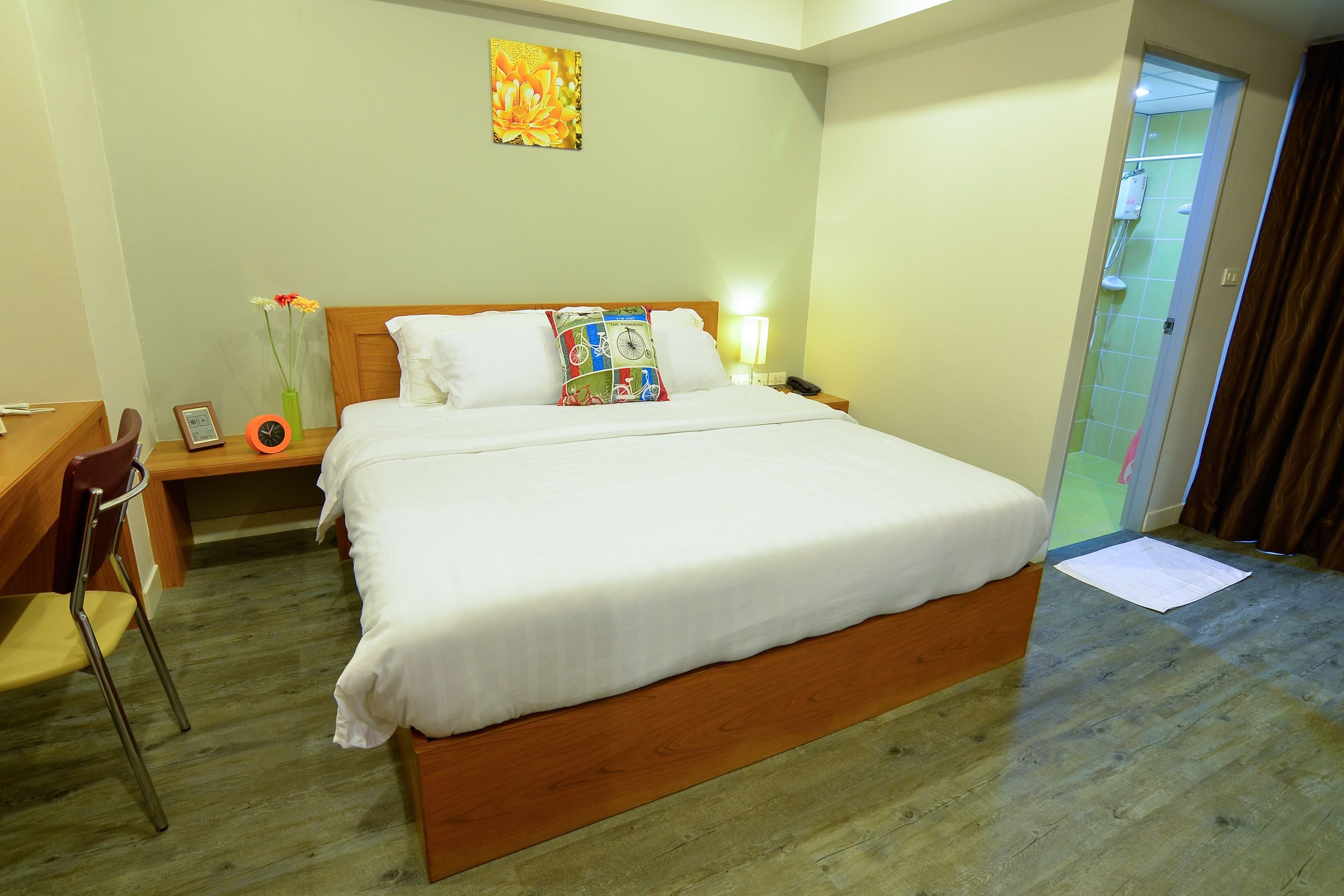 A hotel room with a large bed, a wooden headboard, a bedside table with a lamp, a chair, and a desk.