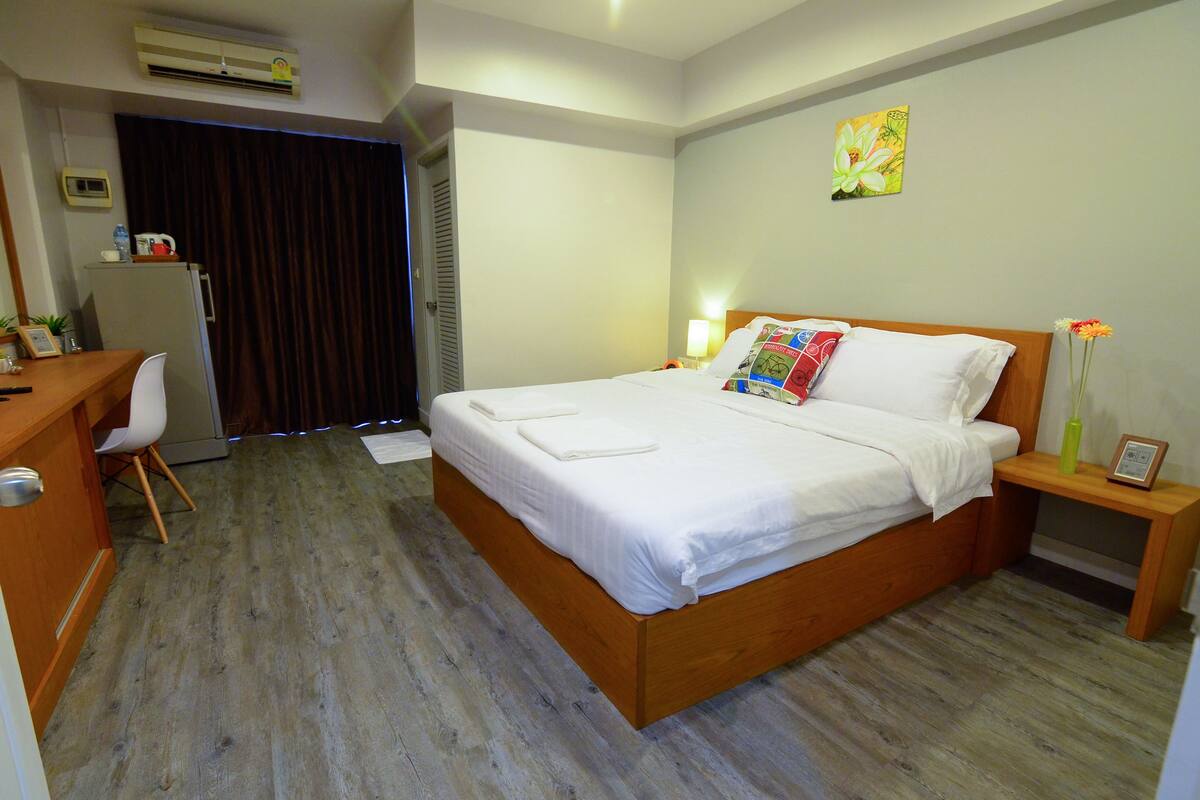 Habitación de hotel con cama de madera, escritorio, silla, refrigerador pequeño y aire acondicionado instalado en la pared.