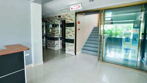 A reception area with a counter, a fire exit sign, a staircase, and a water dispenser. - BJ Boutique (Rayong)