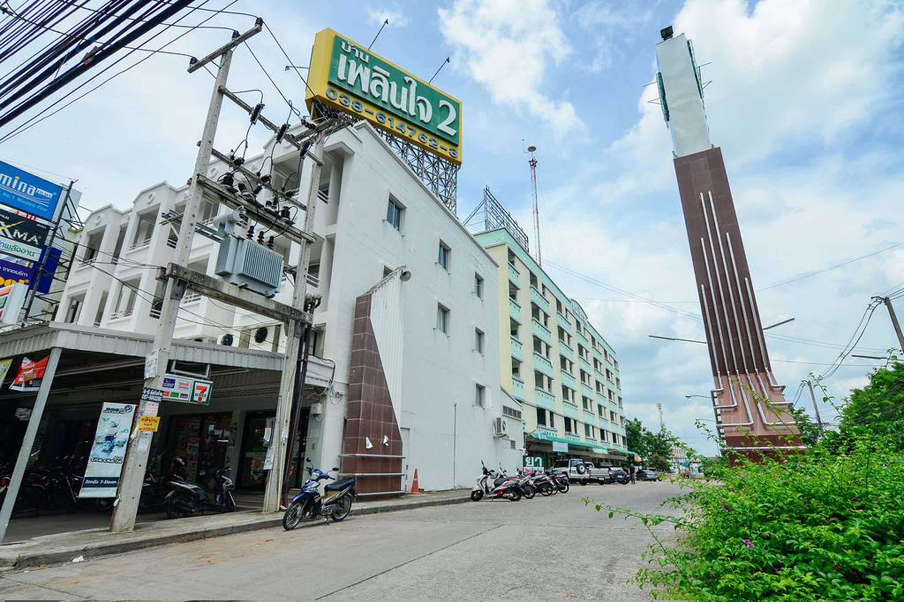 A multi-story building with a prominent vertical structure on the right, a 7-Eleven convenience store on the left, and several parked motorcycles in front.
