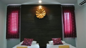 A hotel room with two beds, red curtains, a decorative wall piece, and an air conditioning unit.