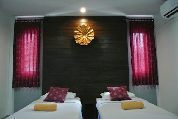 A hotel room with two beds, red curtains, a decorative wall piece, and an air conditioning unit.