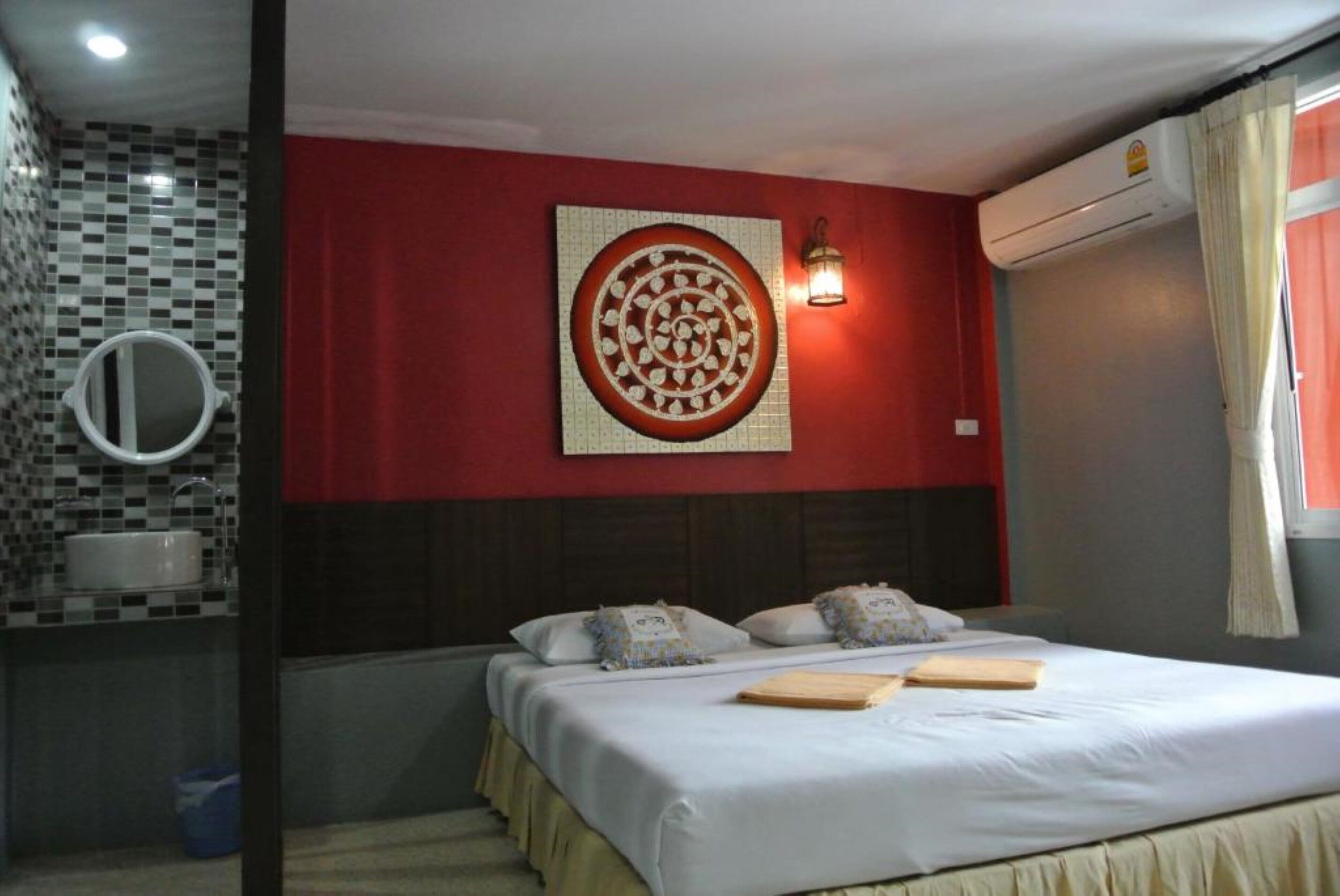 Una habitación de hotel con una cama, un espejo adosado a la pared, un adorno mural, una mesita de noche y una ventana con cortinas.