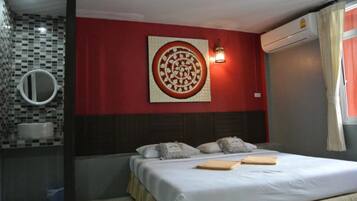Una habitación de hotel con una cama, un espejo adosado a la pared, un adorno mural, una mesita de noche y una ventana con cortinas.