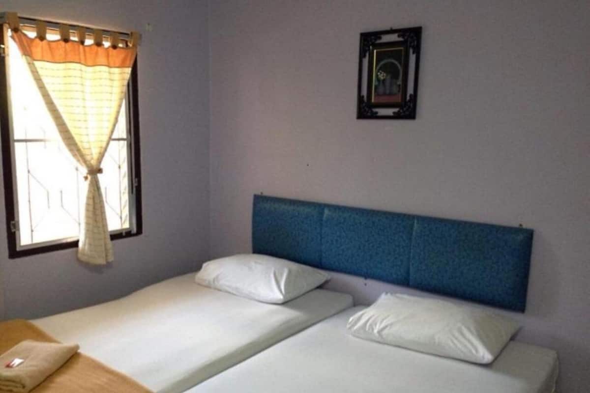 Een kamer met twee eenpersoonsbedden, een raam met gordijnen, een fotolijst aan de muur en een klein tafeltje met een handdoek.