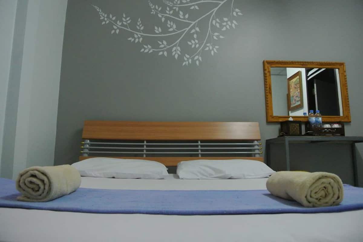 Een keurig opgemaakt bed met twee opgerolde handdoeken, een houten hoofdbord, een spiegel en een muur met een bladmotief.