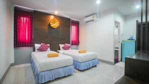 A hotel room with two beds, a wooden headboard, red curtains, an air conditioning unit, a small desk, and a bathroom door.
