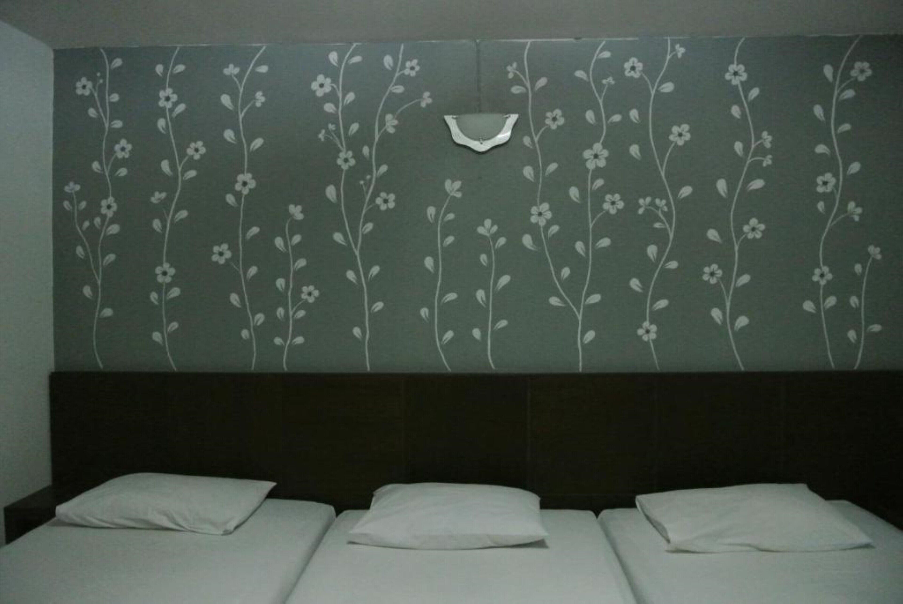 A hotel room with a bed, a headboard, and a wall with a floral pattern.