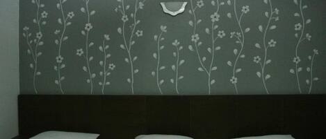 A hotel room with a bed, a headboard, and a wall with a floral pattern.