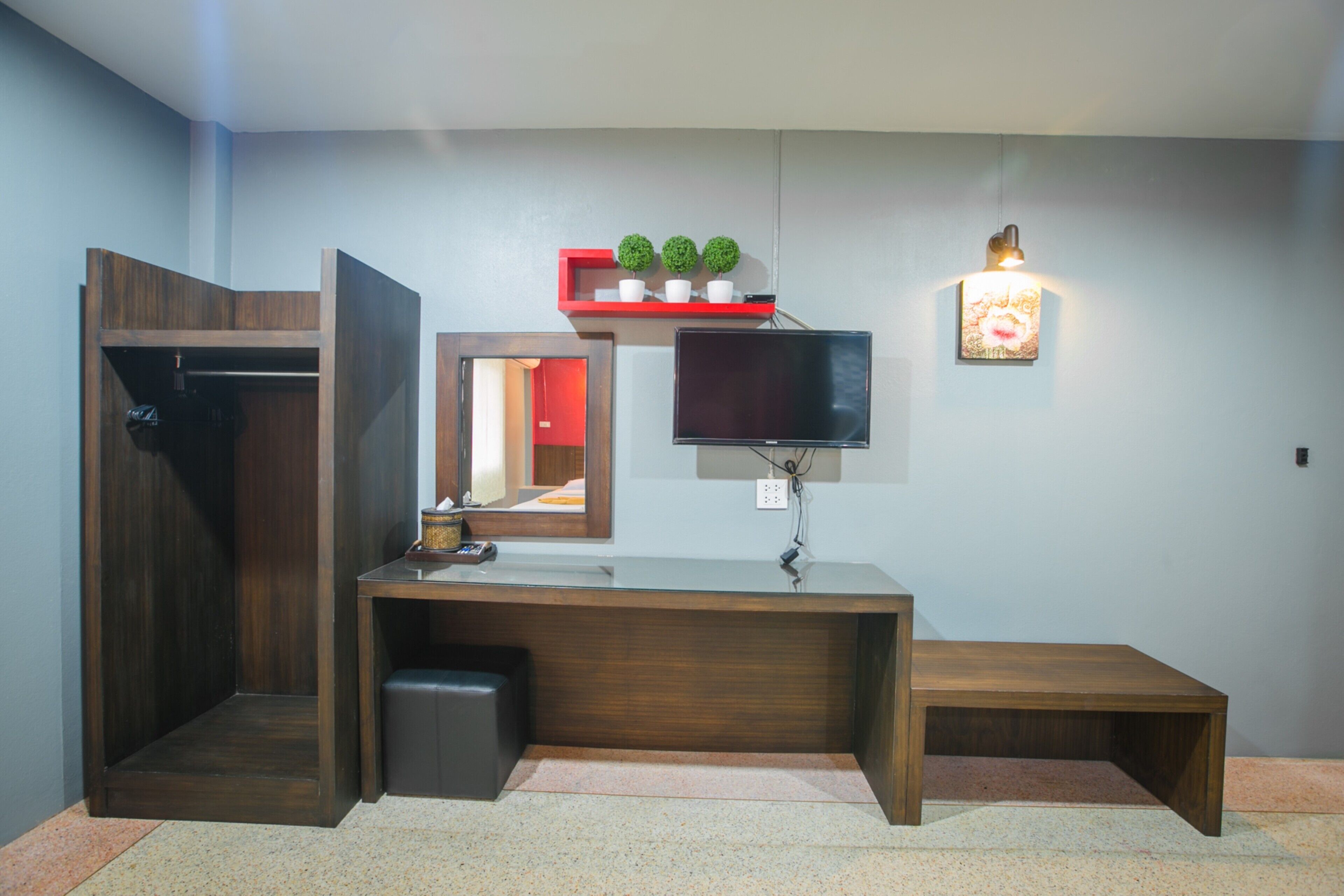 A room with a wooden desk, a TV, a shelf with plants, and a bench.
