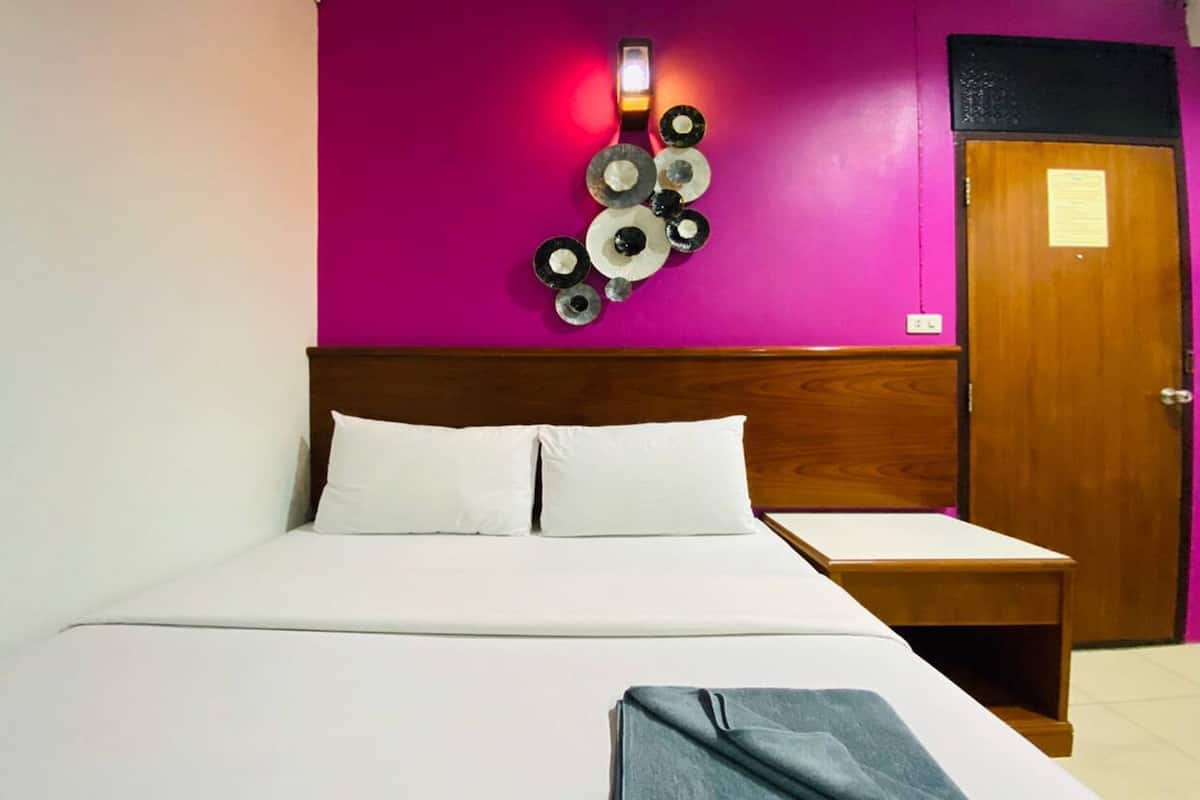 Een hotelkamer met een bed, een houten hoofdbord, een nachtkastje en een wandlamp.
