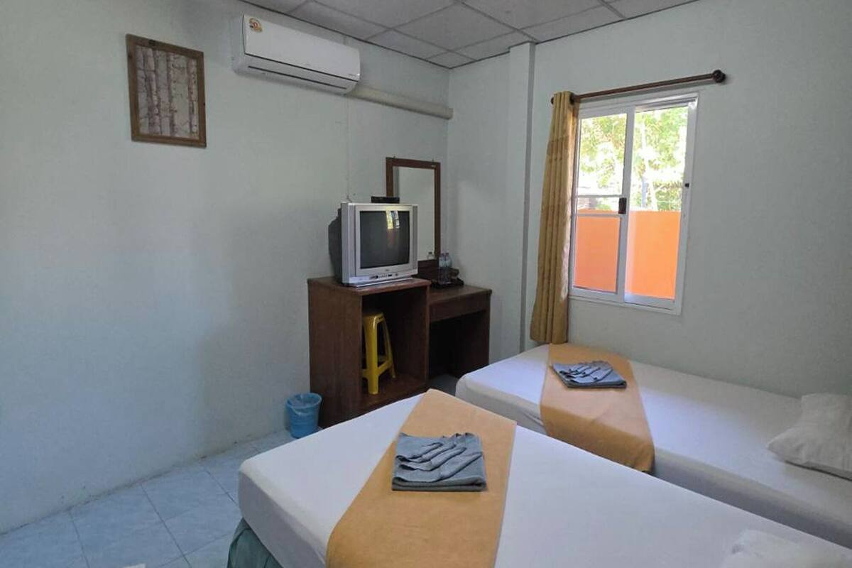 Een hotelkamer met twee bedden, een bureau met een televisie, een airconditioner en een raam met gordijnen.