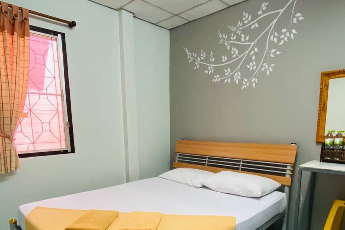 Een enkel bed met houten hoofdeinde, een nachtkastje en een raam met gordijnen.