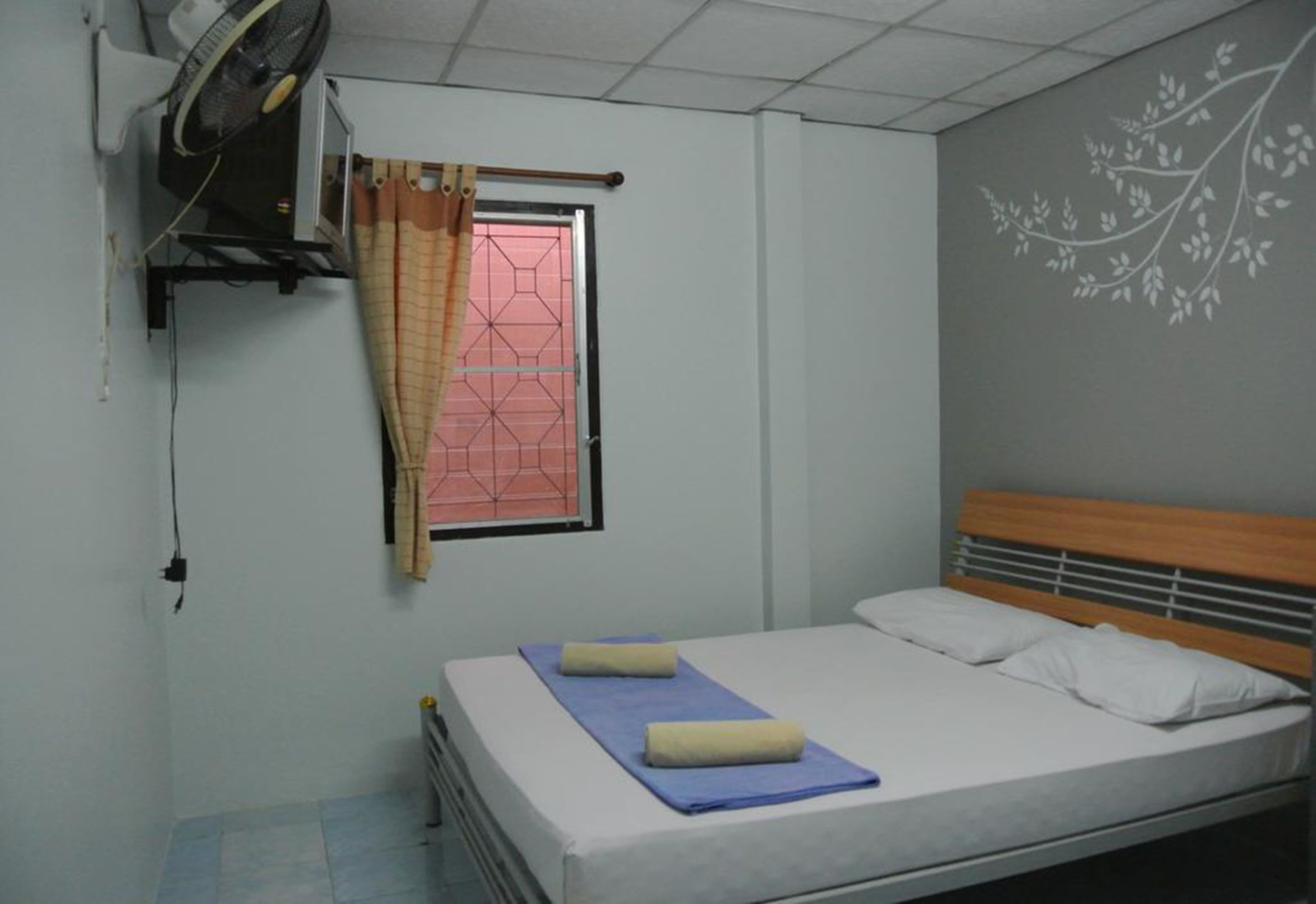Uma cama de solteiro com cabeceira de madeira, janela com cortina e parede com design floral.