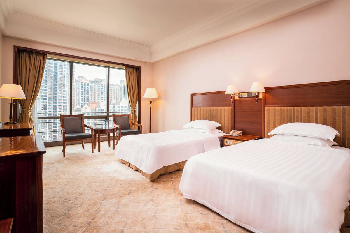 Habitación de hotel con dos camas, un escritorio, una silla y vistas a edificios altos.