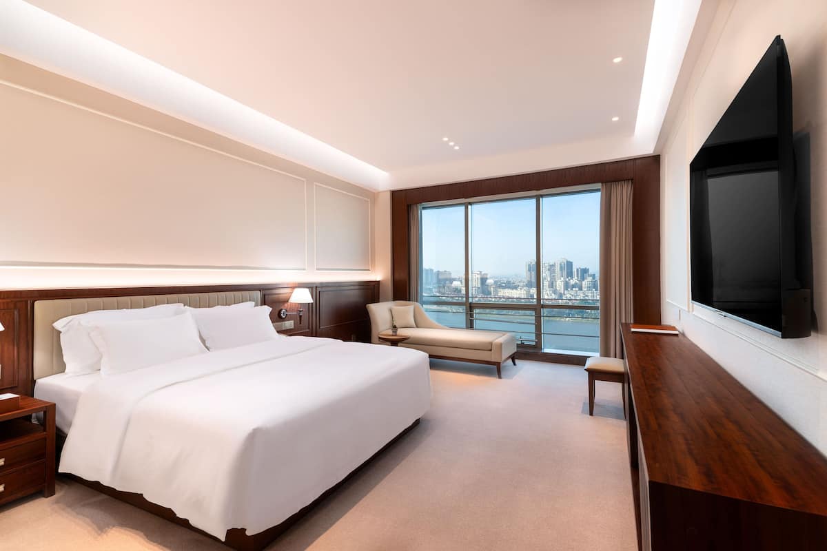 Habitación de hotel moderna con una cama grande, zona de estar, televisión y vistas a la ciudad.