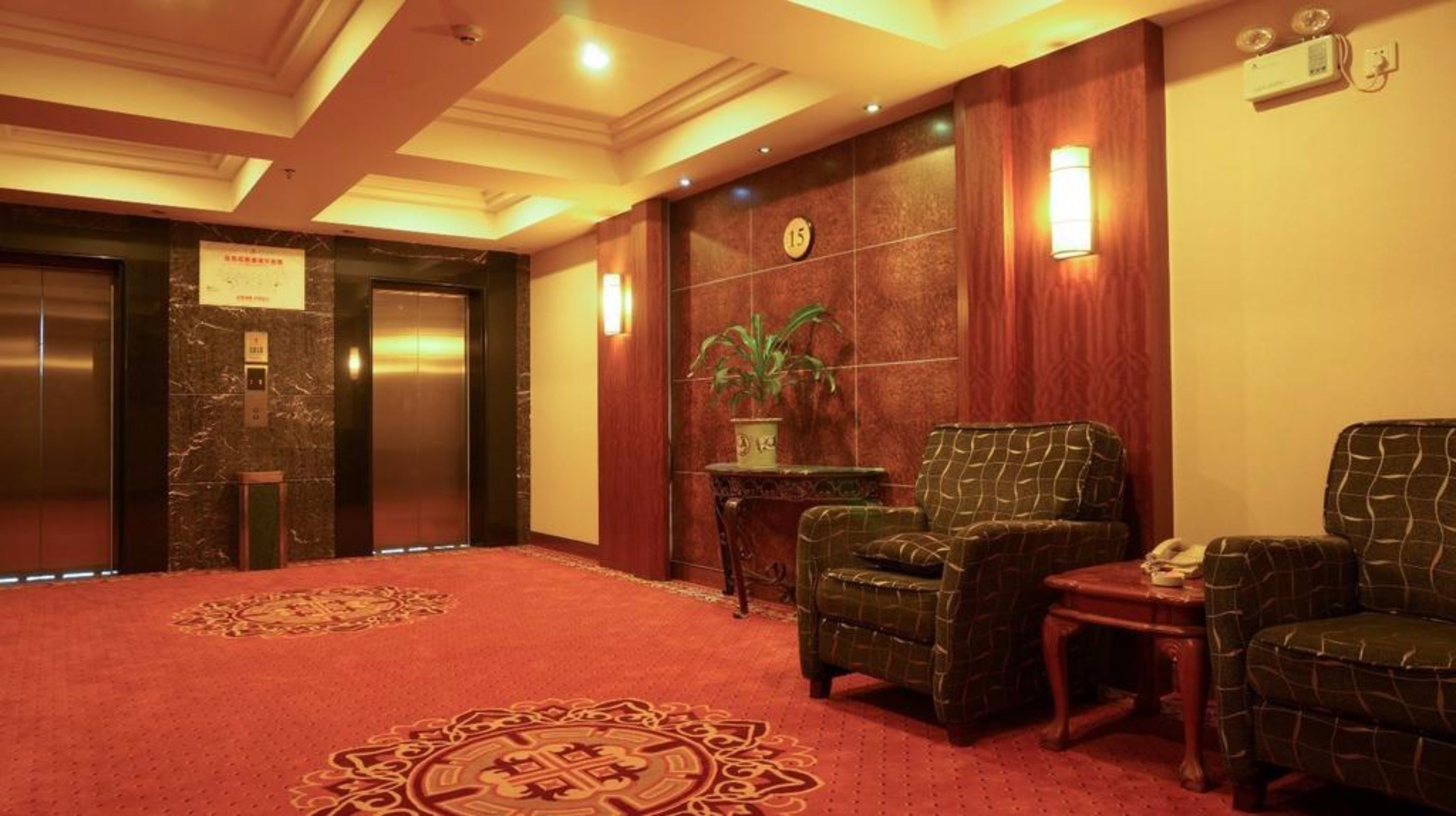 A lobby with a red carpet, two elevators, a reception desk, and a potted plant.