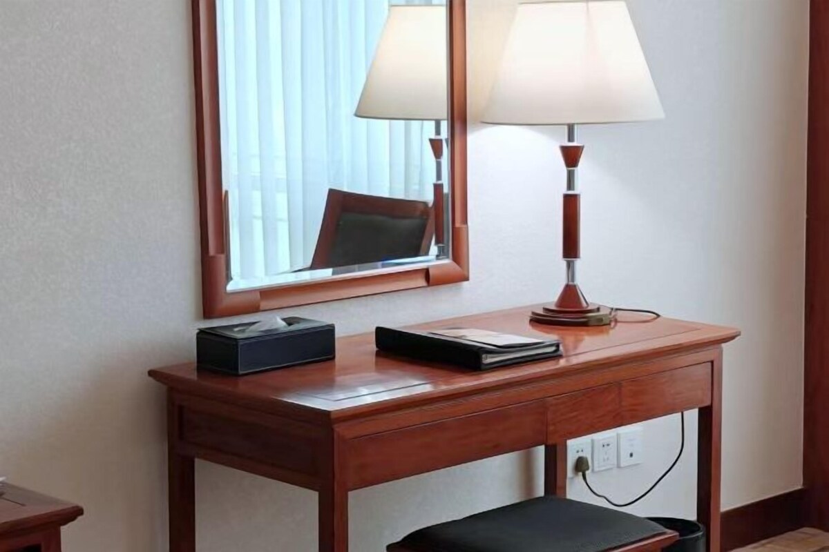 Escritorio de habitación de hotel con una lámpara, un espejo y una mesita con una caja y una libreta.