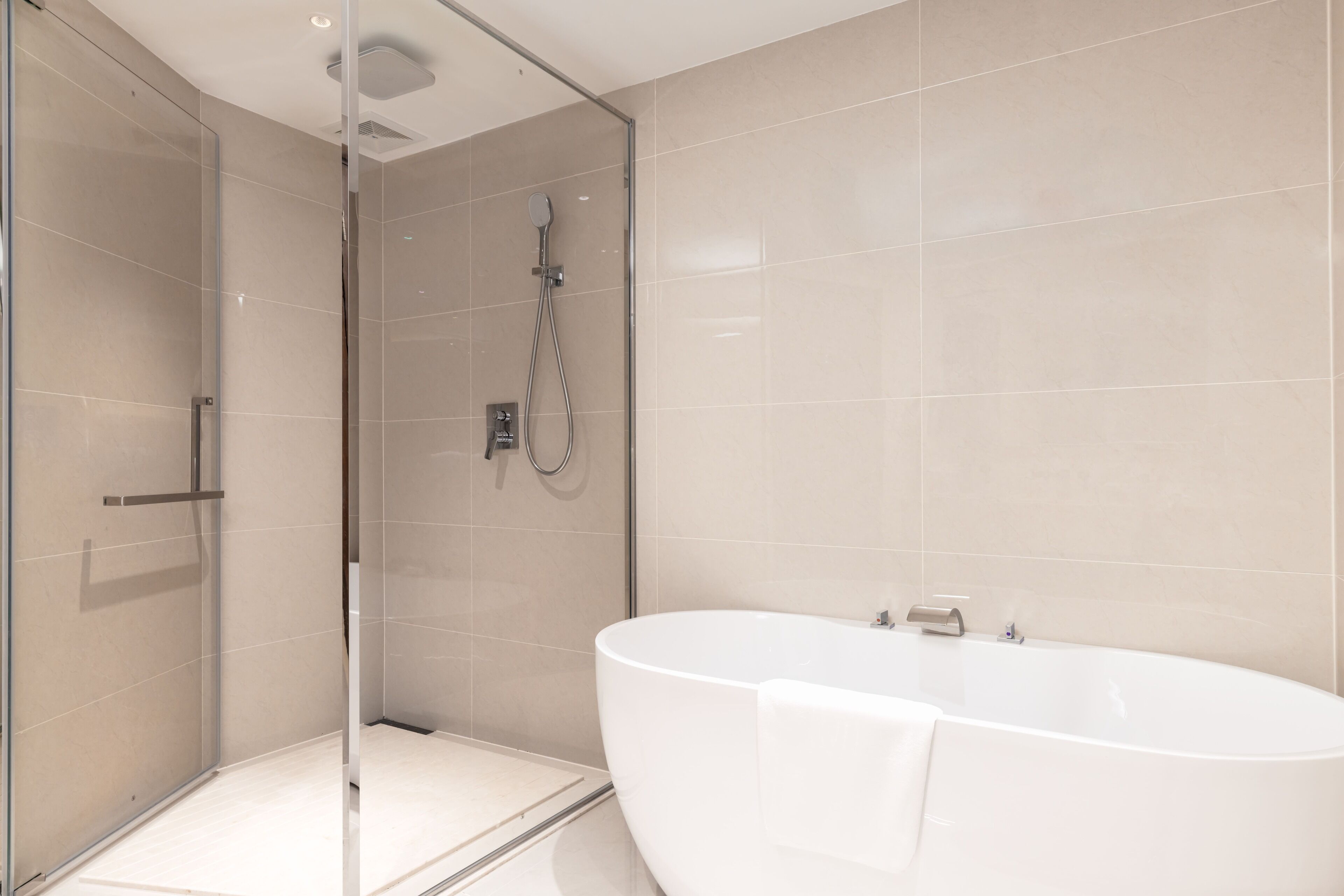 A modern bathroom with a glass-enclosed shower, a freestanding bathtub, and tiled walls.