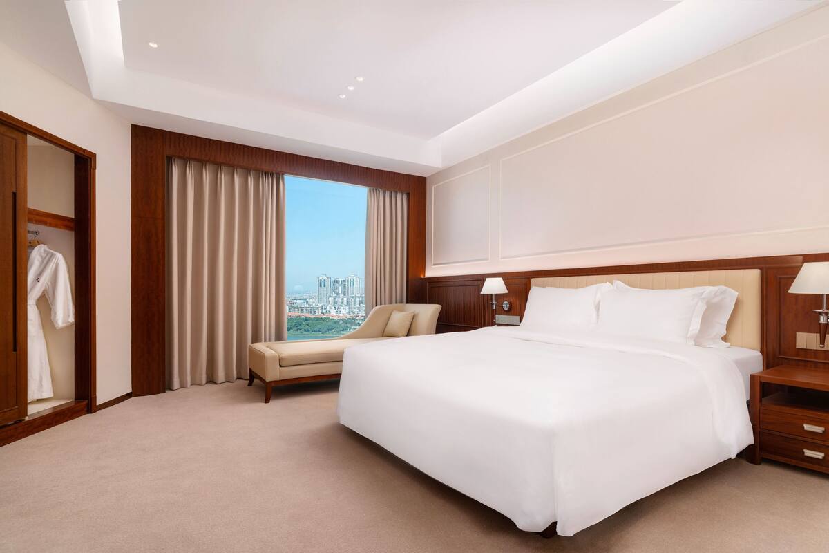 Habitación de hotel con una cama grande, zona de estar, armario y vistas a la ciudad.