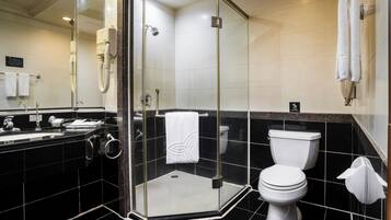 A modern bathroom with a glass-enclosed shower, a white toilet, and a black-tiled sink area.
