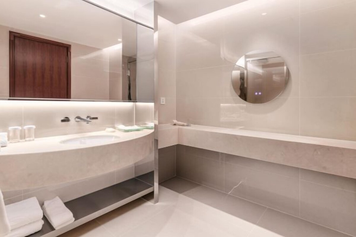 Un baño moderno con un espejo grande, un lavamanos y un espejo redondo en la pared.