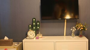 A television mounted on a wall, a clock, a cactus, a vase with flowers, and a tissue box on a dresser. - Woosung Hotel (Seogwipo)