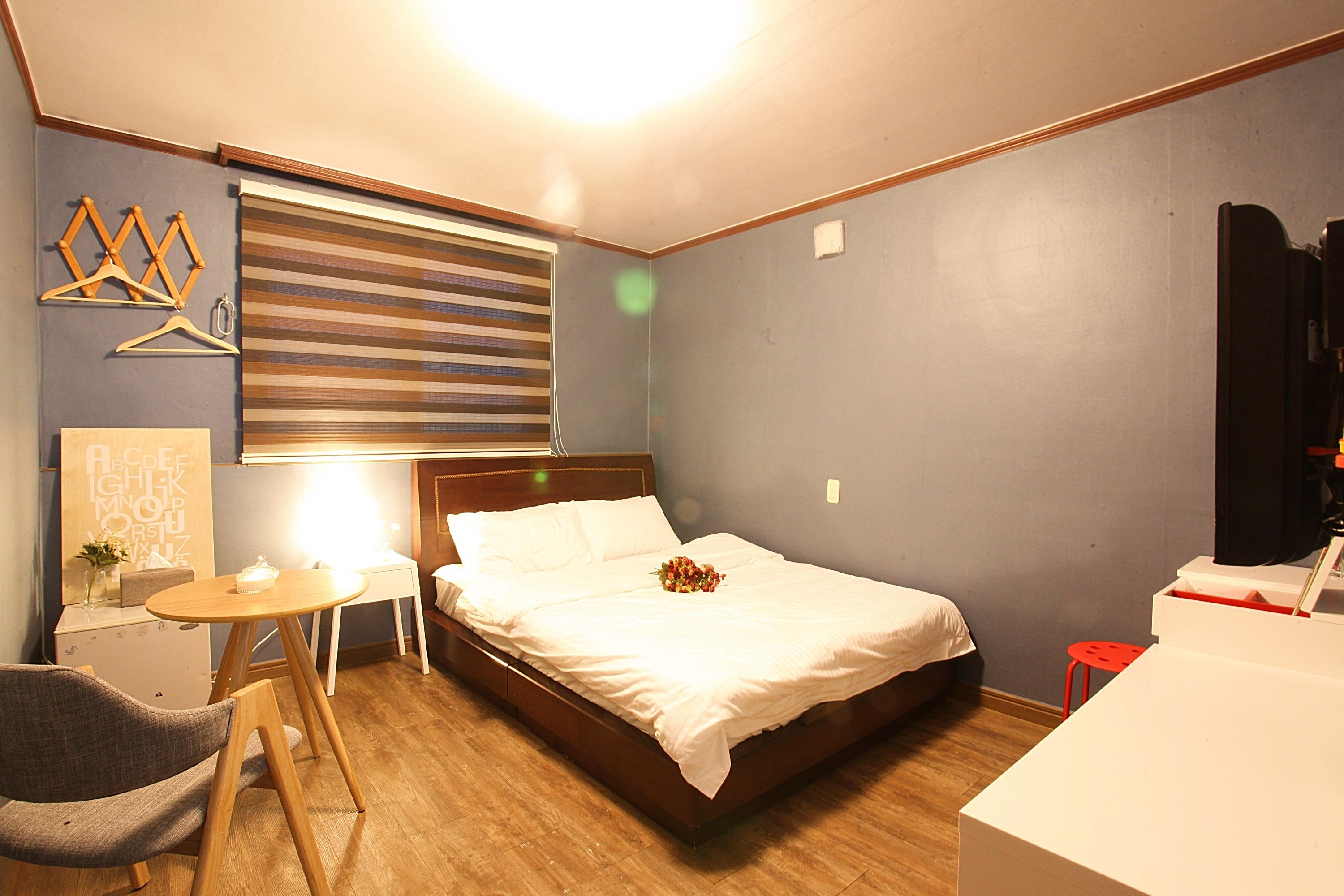 A bedroom with a bed, a desk, a chair, a small table, and a window with blinds.