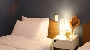 A neatly made bed with white linens, a bedside table with a lamp, a clock, and a bouquet of flowers. - Woosung Hotel (Seogwipo)