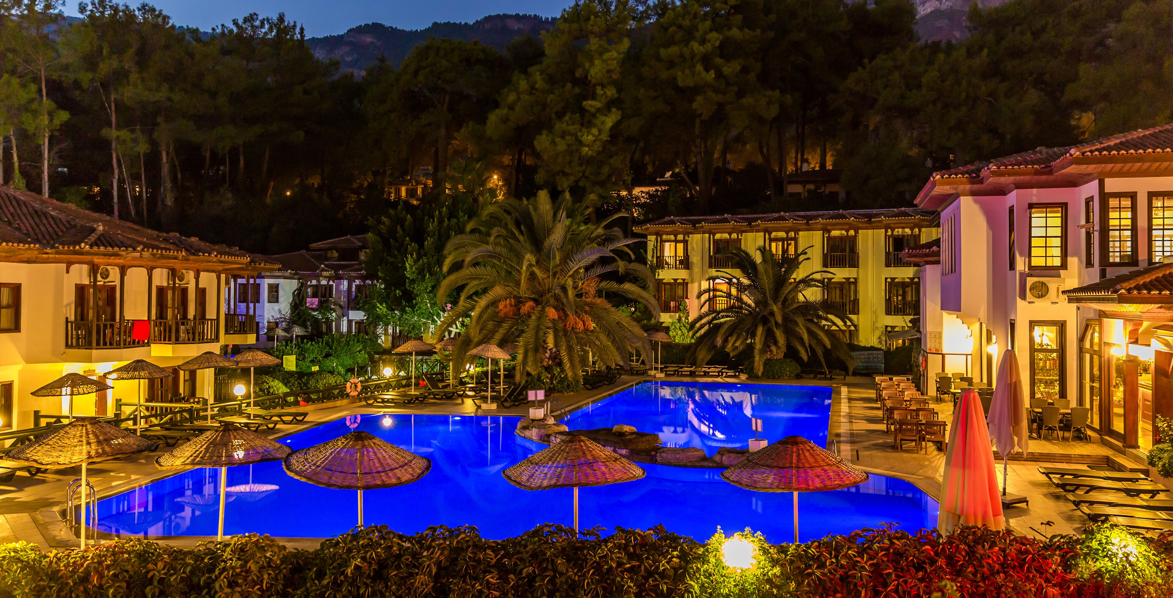 A swimming pool with umbrellas, lounge chairs, and a view of surrounding buildings.