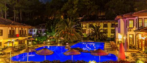 A swimming pool with umbrellas, lounge chairs, and a view of surrounding buildings.