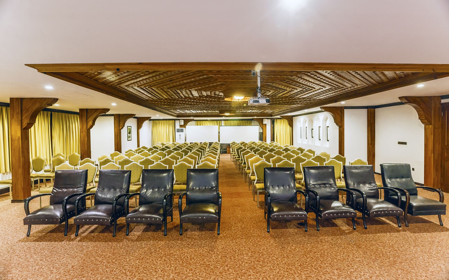 A conference room with rows of chairs, a projector, and a carpeted floor.