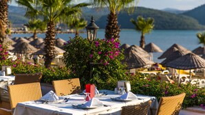 Mesa preparada para comer con vista al mar y montañas al fondo.