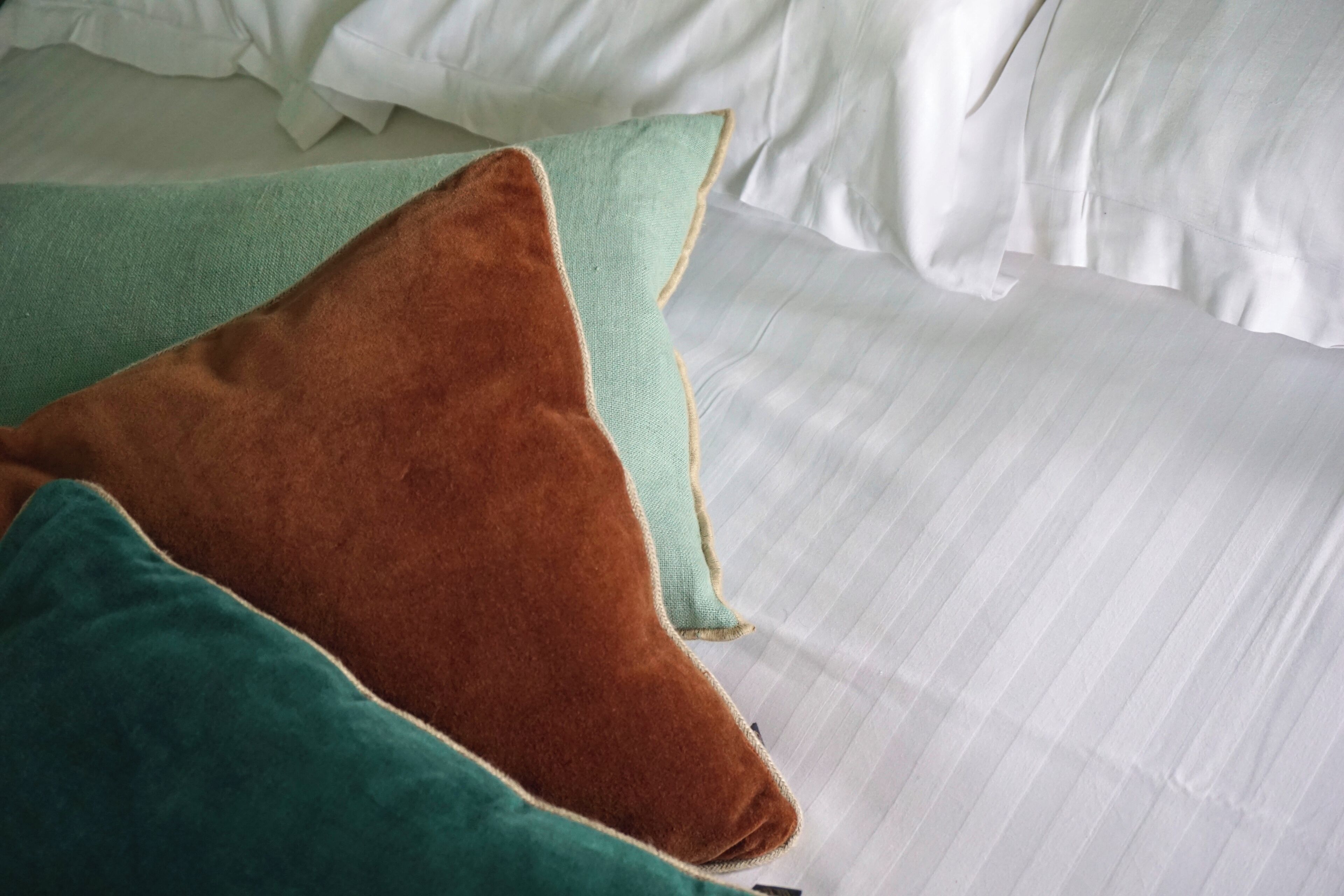 Una cama con sábanas blancas y tres almohadas de distintos colores.