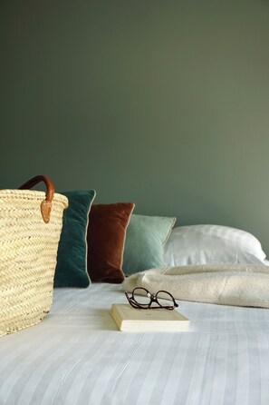A bed with striped bedding, a woven bag, and a book with glasses on it. - Hôtel les Bains (Saint-Valery-en-Caux)